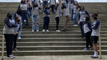 Students standing on stairs posing for a picture, 3 students make "UCD" using their arms